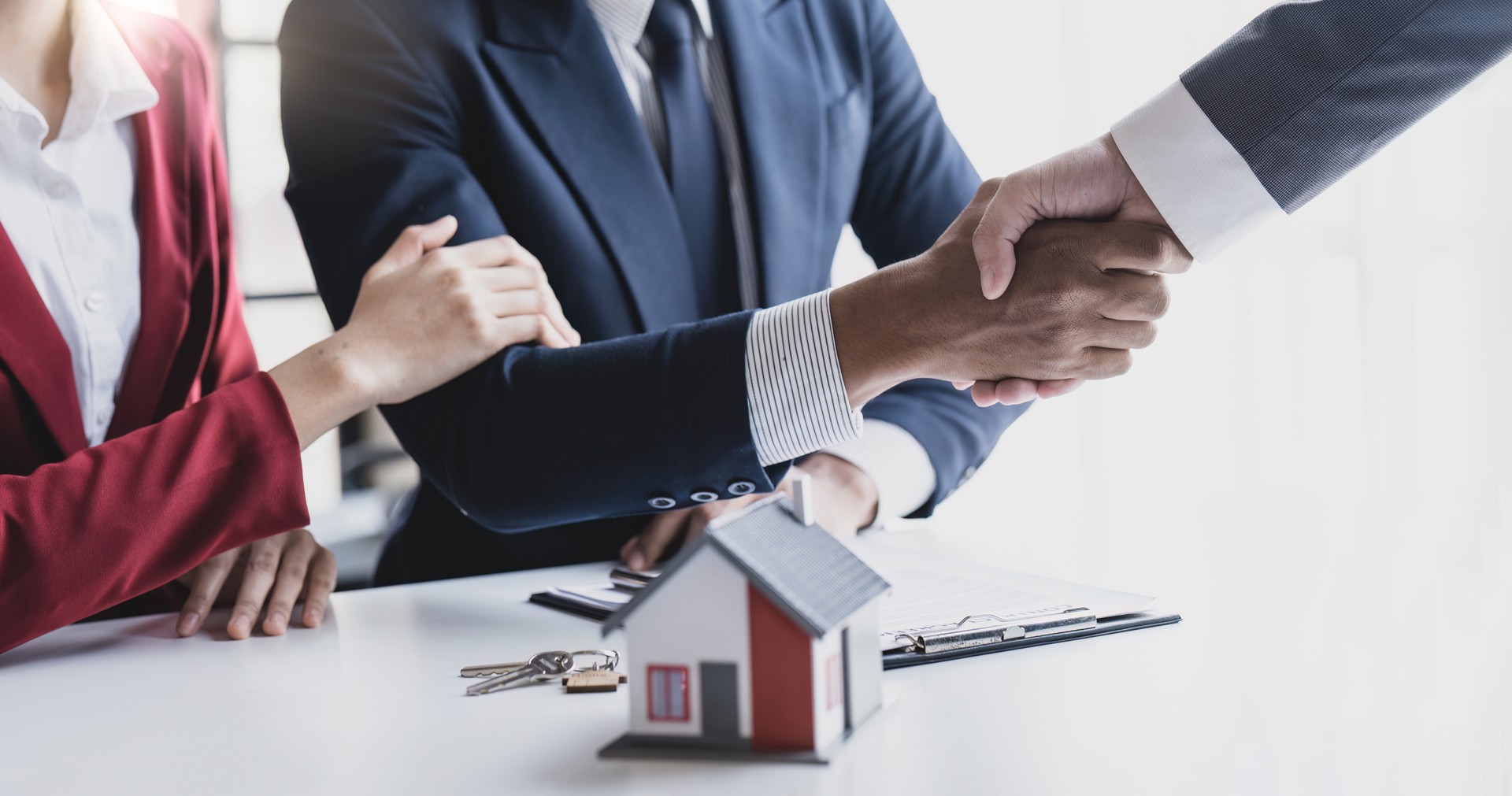 Good deal buy new house Cheerful young man bonding to his wife while shaking hand to man sitting in front of him at office.